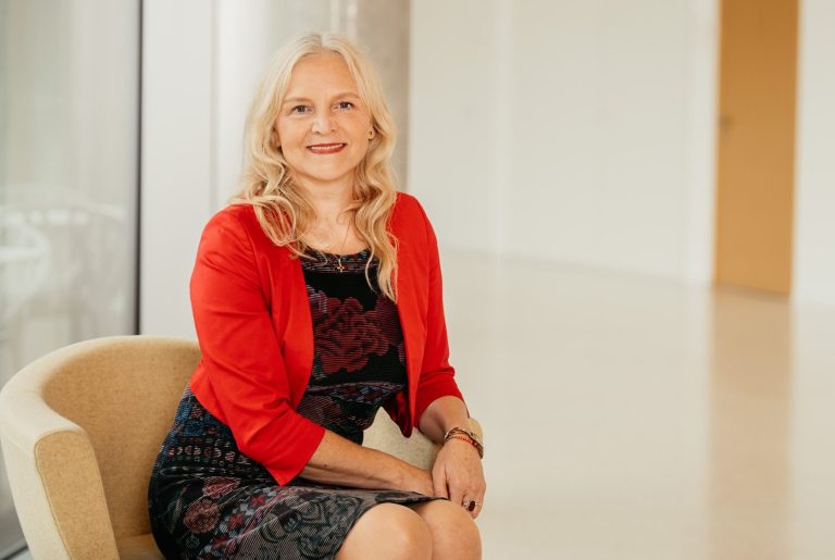 Porträt einer Frau mit langen blonden Haaren und einer roten Jacke.